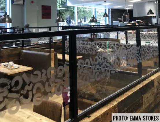 A picture of the Morries cafe: in the bottom right corner is a caption: 'PHOTO: EMMA STOKES'. Behind a row of glass panes in an assortment of tables: some with normal chairs and some with sofa benches.