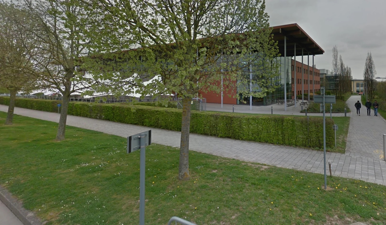 A view of the Cambridge Computer Laboratory, partially obscured by trees. Through the trees is a canopied area.